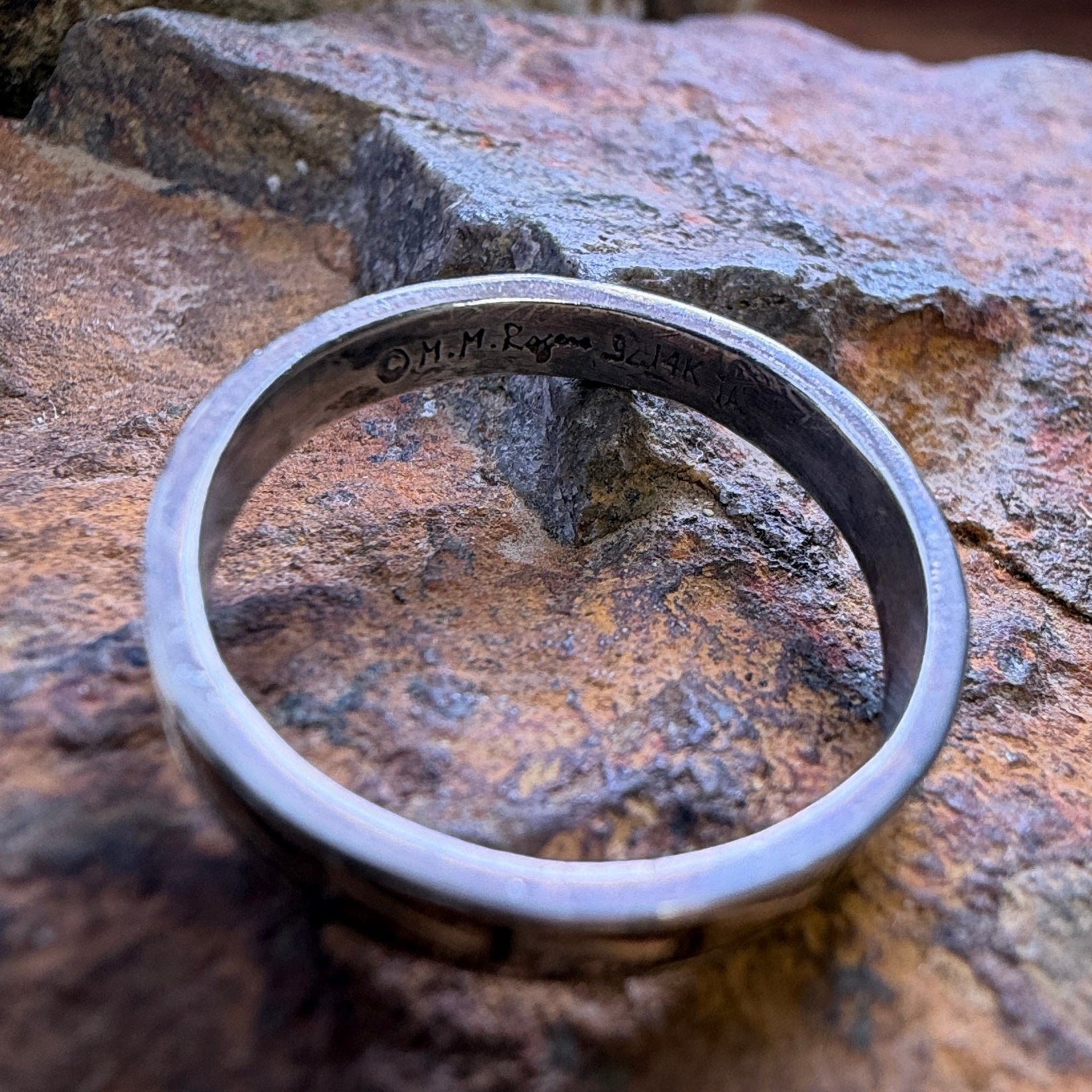A sterling silver and 14k gold ring sitting on a rocky surface showcasing the stamping on the inside