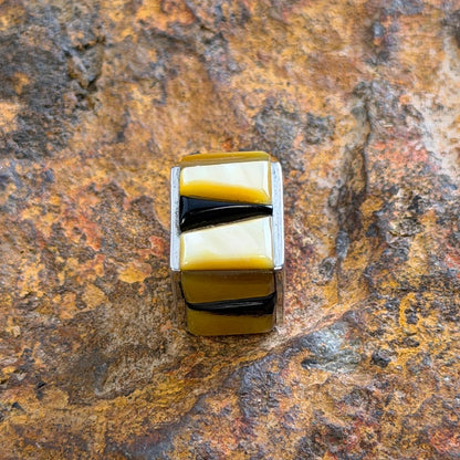 A square pendant with alternating yellow and black striped segments, set in a silver metal, displayed on a textured brown and orange rock surface.