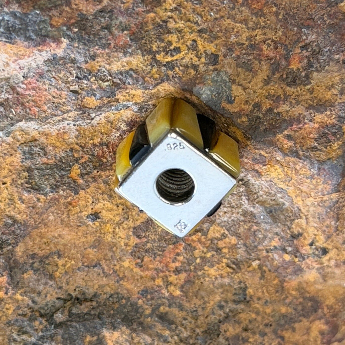 Silver side face of a cobbled cube pendant that features the stamping .825 and hallmark of the artist