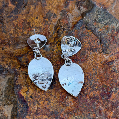 Hammer finished drop earrings by artie yellowhorse. They hang from a piece of driftwood
