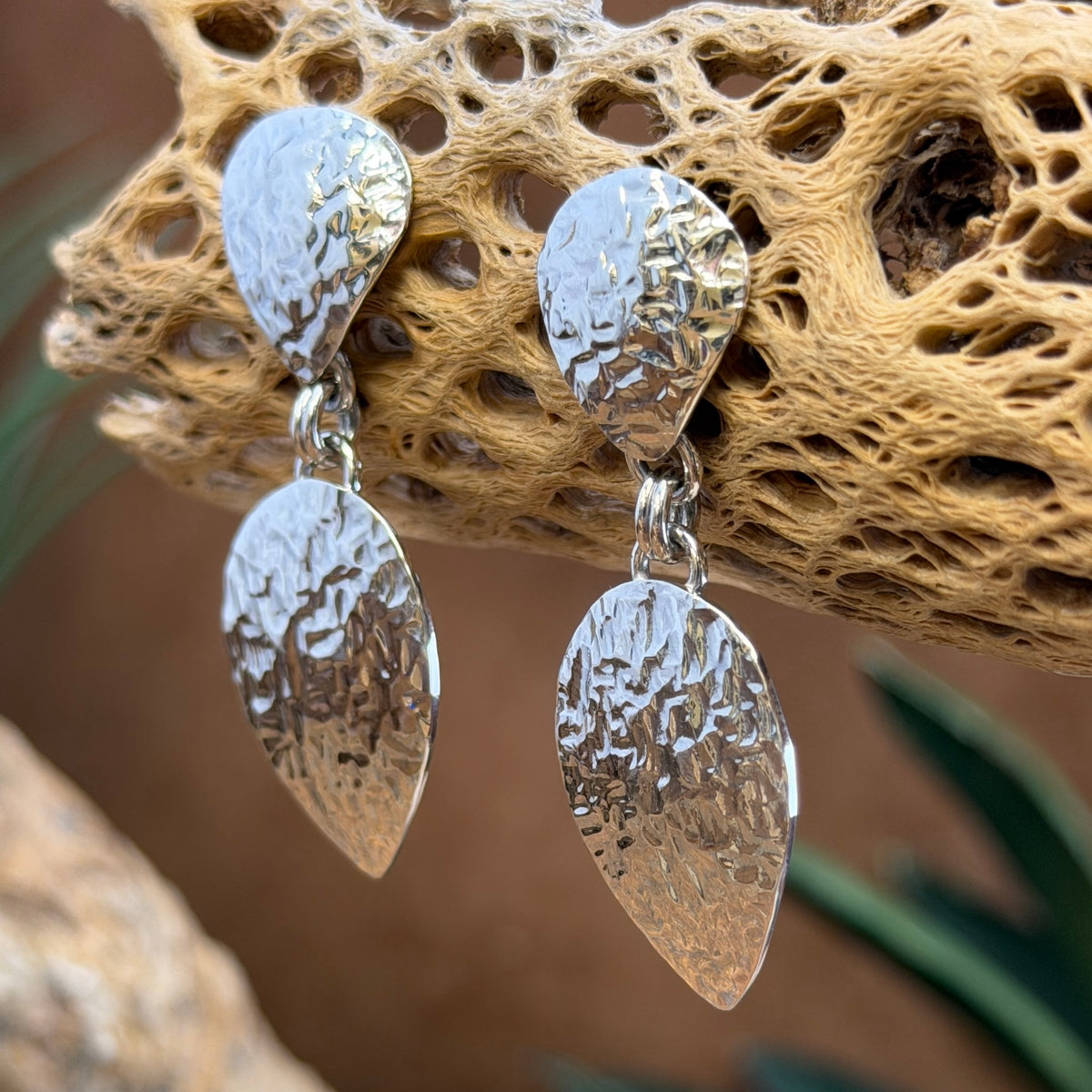 Hammer finished drop earrings by artie yellowhorse. They hang from a piece of driftwood