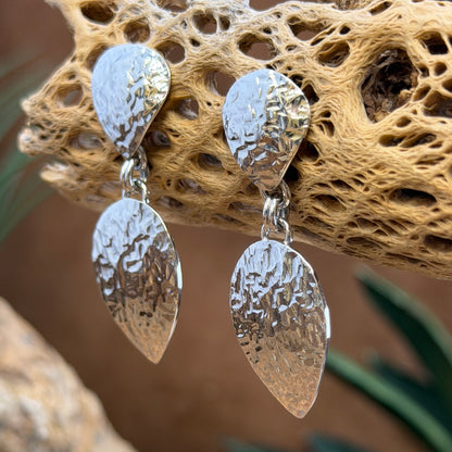 Hammer finished drop earrings by artie yellowhorse. They hang from a piece of driftwood