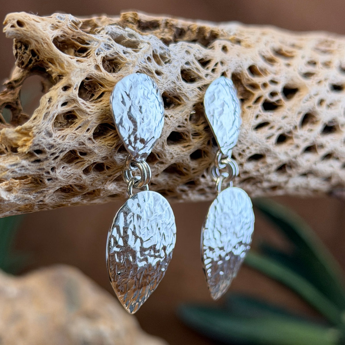 Hammer finished drop earrings by artie yellowhorse. They hang from a piece of driftwood