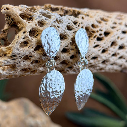 Hammer finished drop earrings by artie yellowhorse. They hang from a piece of driftwood