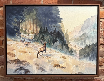 Framed painting of deer in a forest scene on a brick wall.