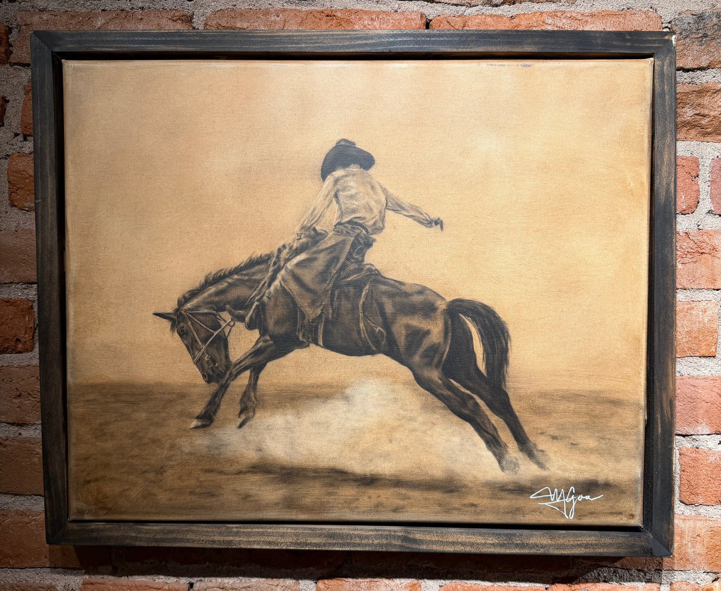 Framed artwork of a person riding a horse on a textured background, displayed against a brick wall.