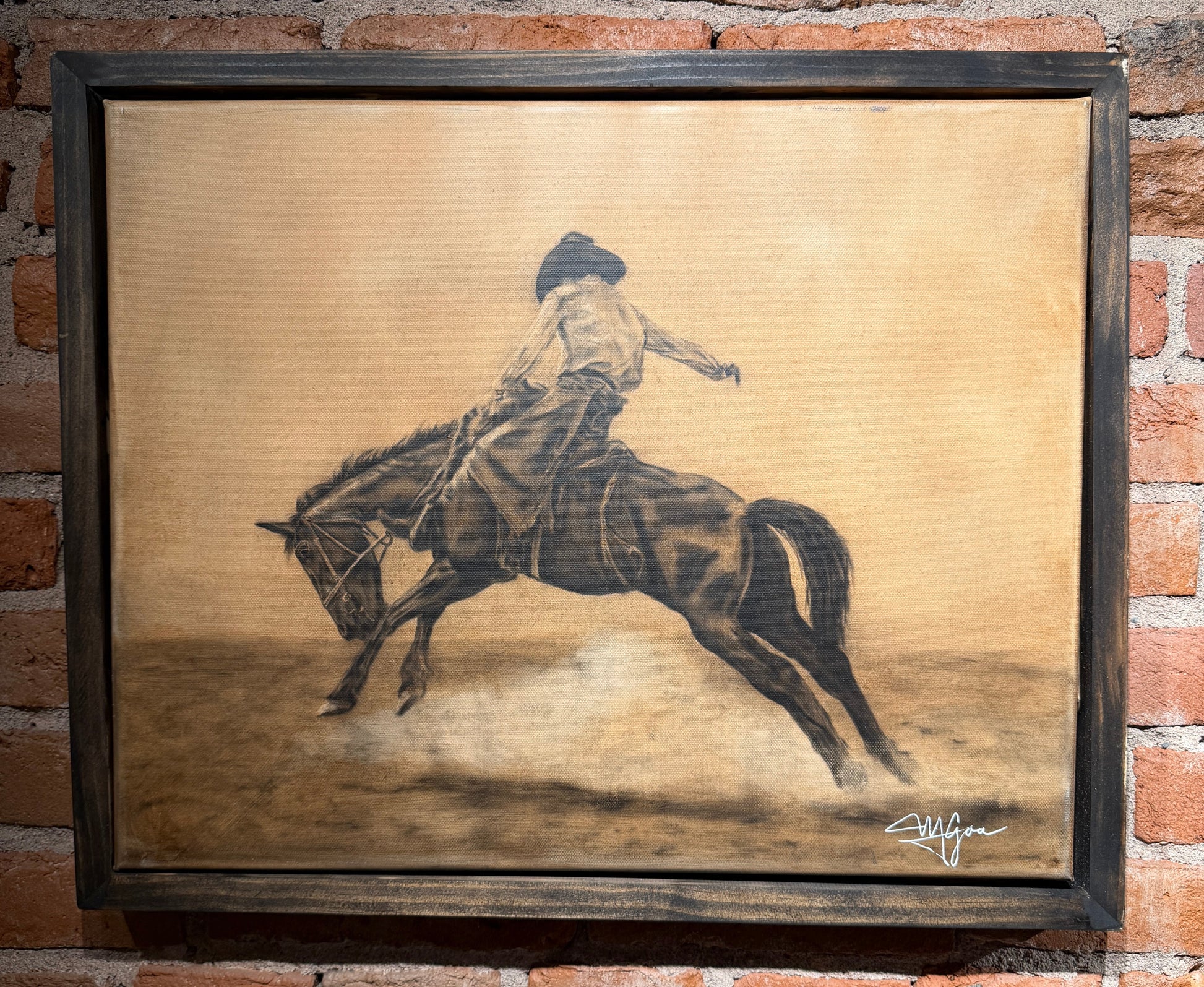 Framed artwork of a person riding a horse on a textured background, displayed against a brick wall.