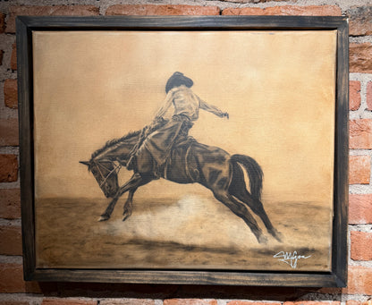 Framed artwork of a person riding a horse on a textured background, displayed against a brick wall.