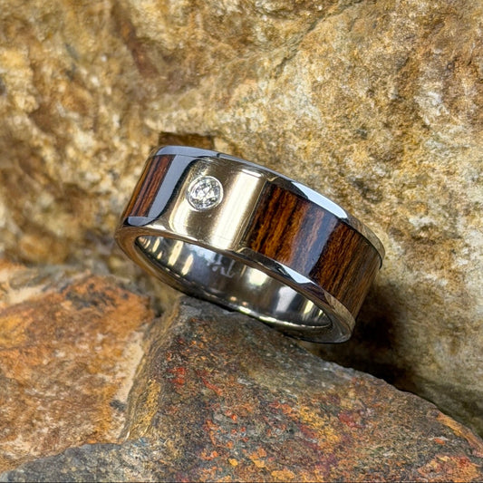 A ring with a dark brown wood inlay and a small clear diamond, resting on textured orange-brown rocks outdoors