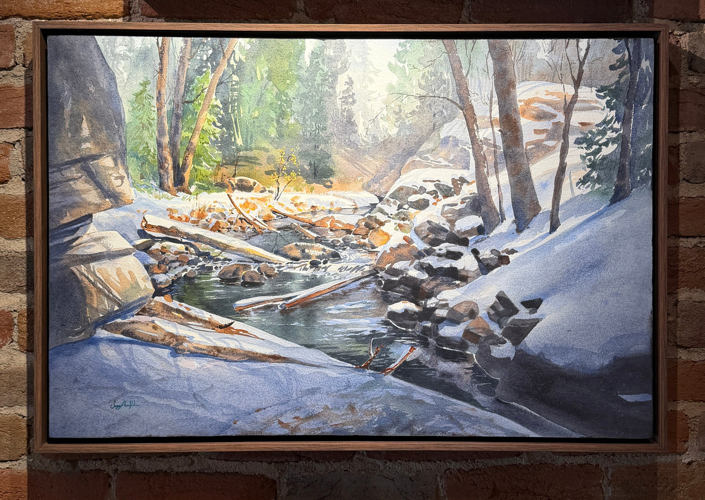 Two framed paintings of landscapes on a brick wall.