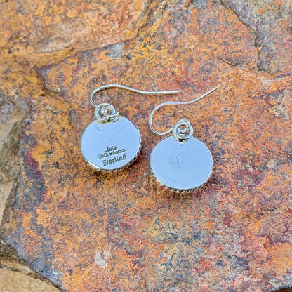 dome earrings with a twisted rope border by artie yellowhorse. they rest on a rocky surface