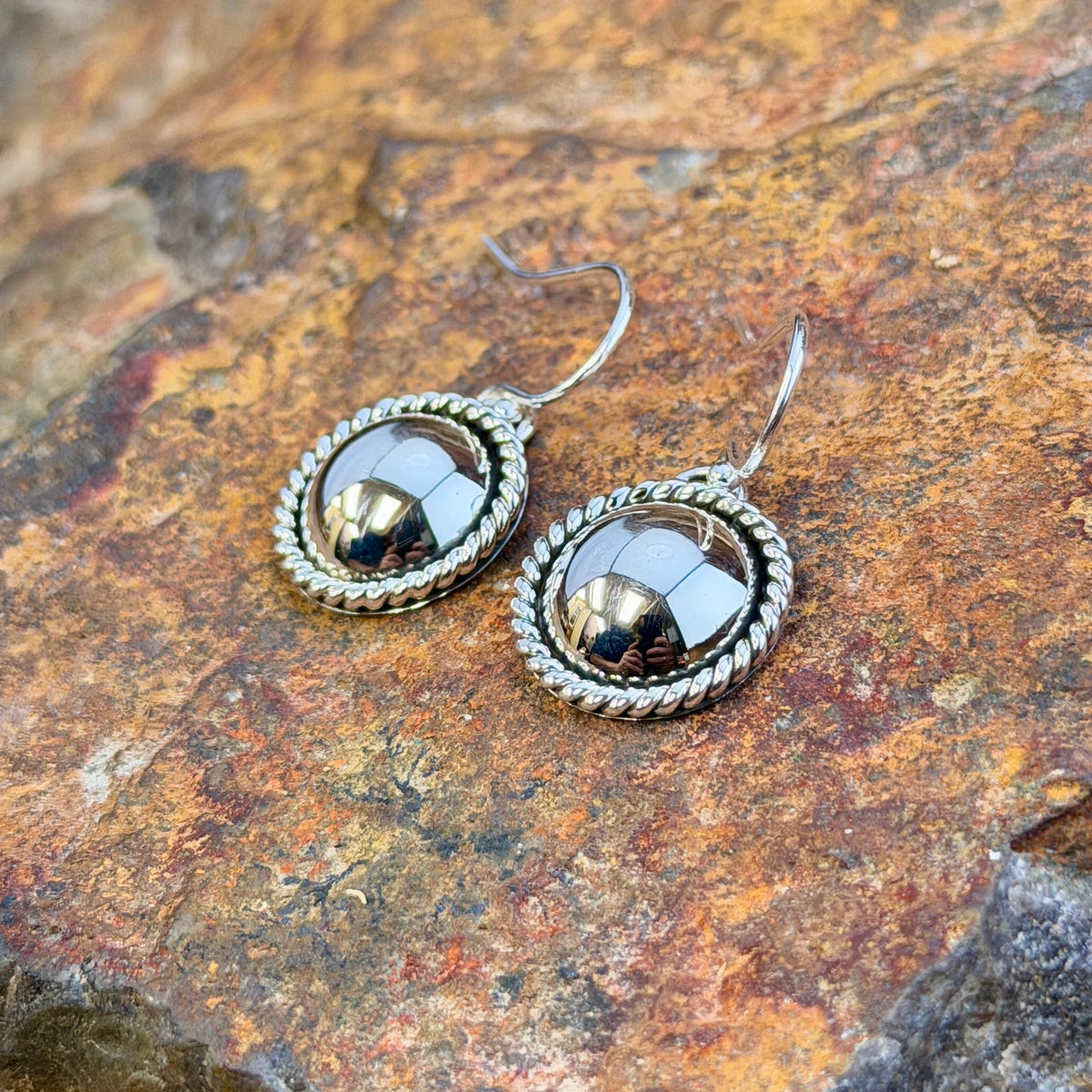 dome earrings with a twisted rope border by artie yellowhorse. they rest on a rocky surface