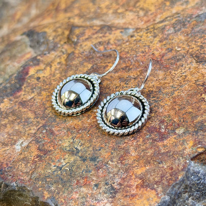 dome earrings with a twisted rope border by artie yellowhorse. they rest on a rocky surface