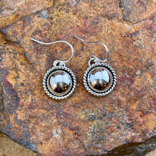 dome earrings with a twisted rope border by artie yellowhorse. they rest on a rocky surface