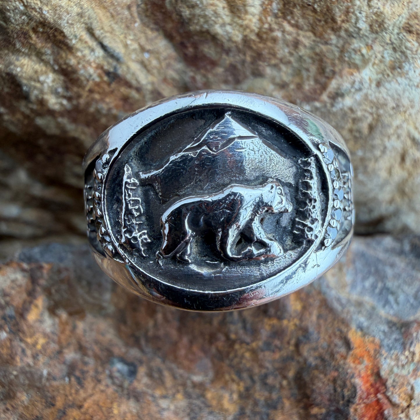 Image of a sterling silver ring with a bear engraving amongst natural scenery 