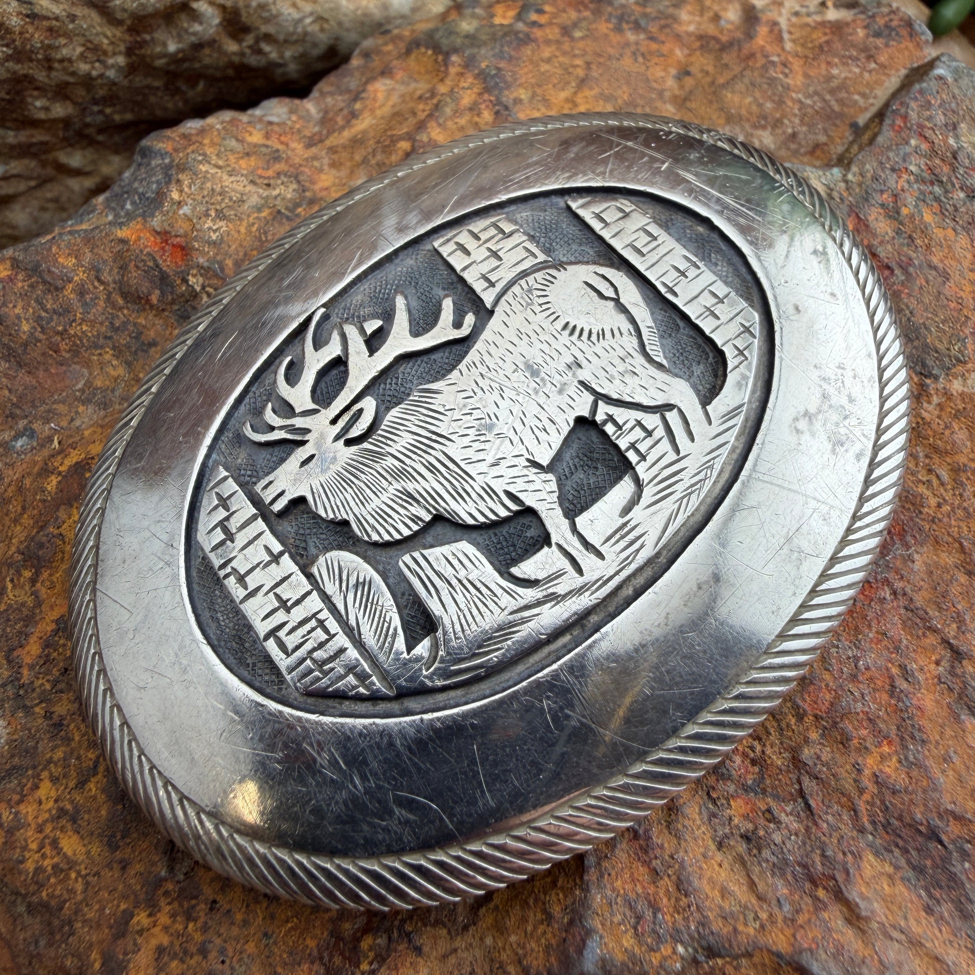 Silver belt buckle with deer design on a stone background