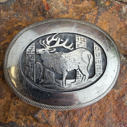 Silver belt buckle with elk design on a stone surface