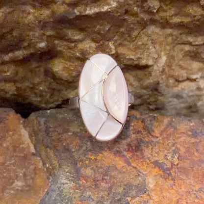 Oval ring face inlaid with light pink segments. nestled in-between a rocky surface