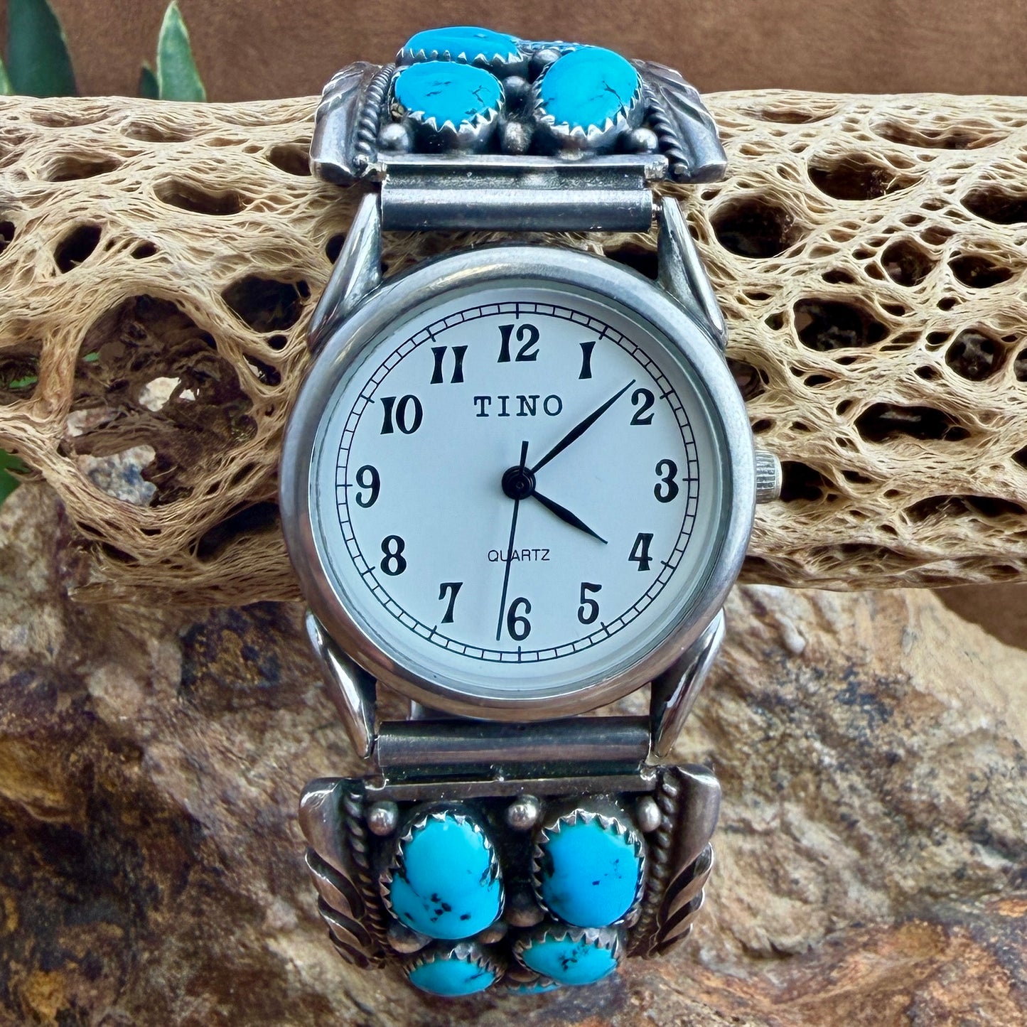A TINO brand silver-toned watch with turquoise stones on the bracelet, resting on a textured natural rock surface.