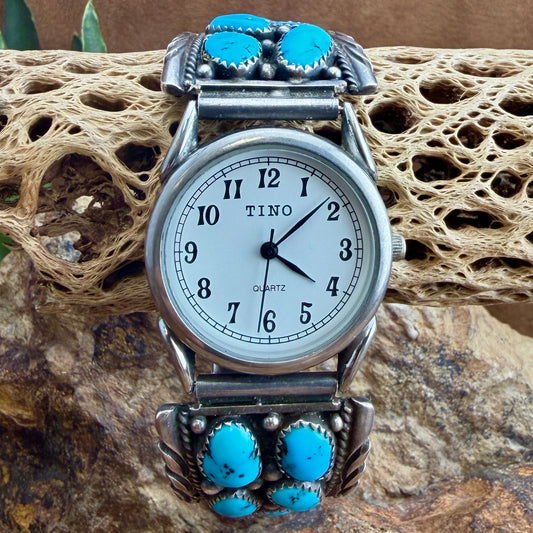 A TINO brand silver-toned watch with turquoise stones on the bracelet, resting on a textured natural rock surface.