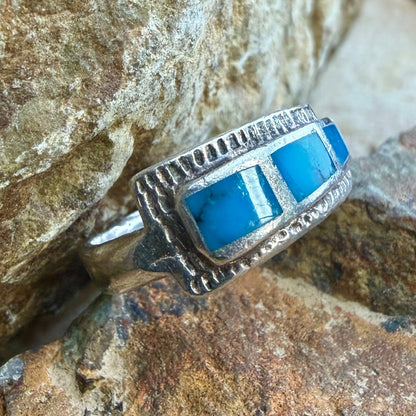 A silver ring with  rectangular blue turquoise inlays, resting on a textured brown and gray rock surface.
