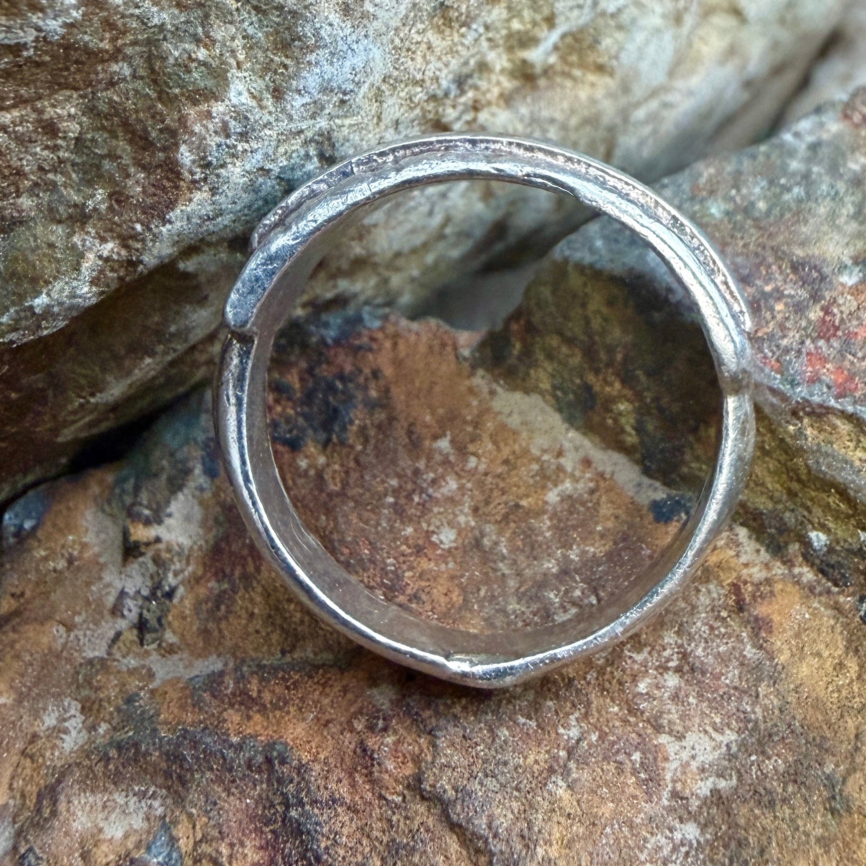 A silver ring, resting on a textured brown and gray rock surface.