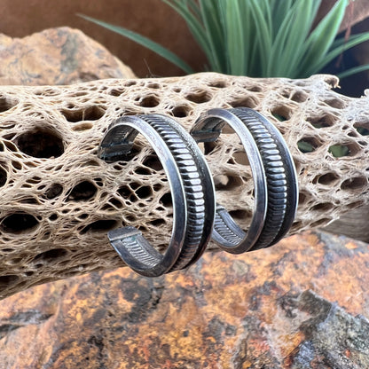 Side view of sterling silver half-hoop earrings featuring a deeply oxidized ribbed center band flanked by smooth, polished rims.