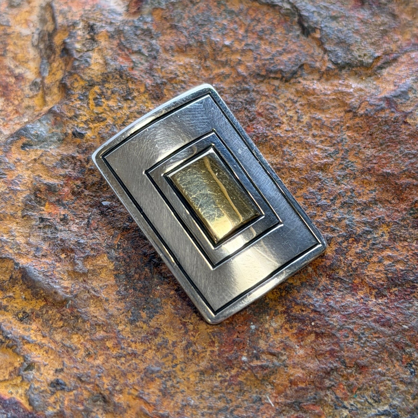A small rectangular pendant with a concentric nestled motif with gold on the inside and silver on the outside
