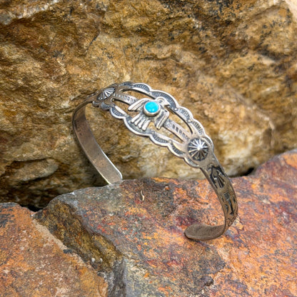 A silver-toned Southwestern-style cuff bracelet with a turquoise stone, displayed on textured orange and brown rocks.