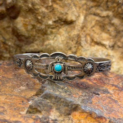 A silver-toned Southwestern-style bracelet with a small turquoise stone, resting on a textured orange-brown rock surface.