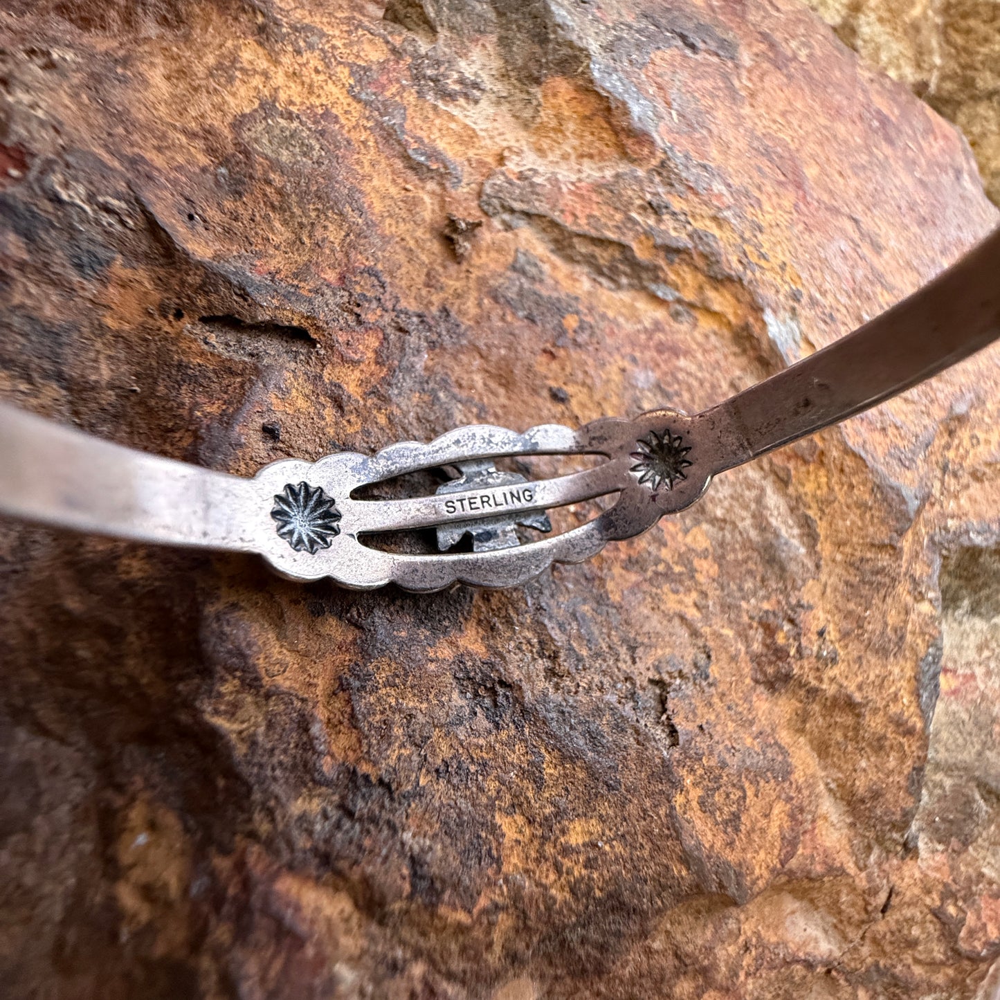 the inside of sterling silver cuff bracelet with floral starburst details, shown resting on a textured brown rock surface. stamped "Sterling"