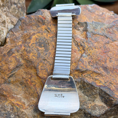  the back of a A sterling silver and 14k gold watch band displayed on a textured tan branch with a natural outdoor background.