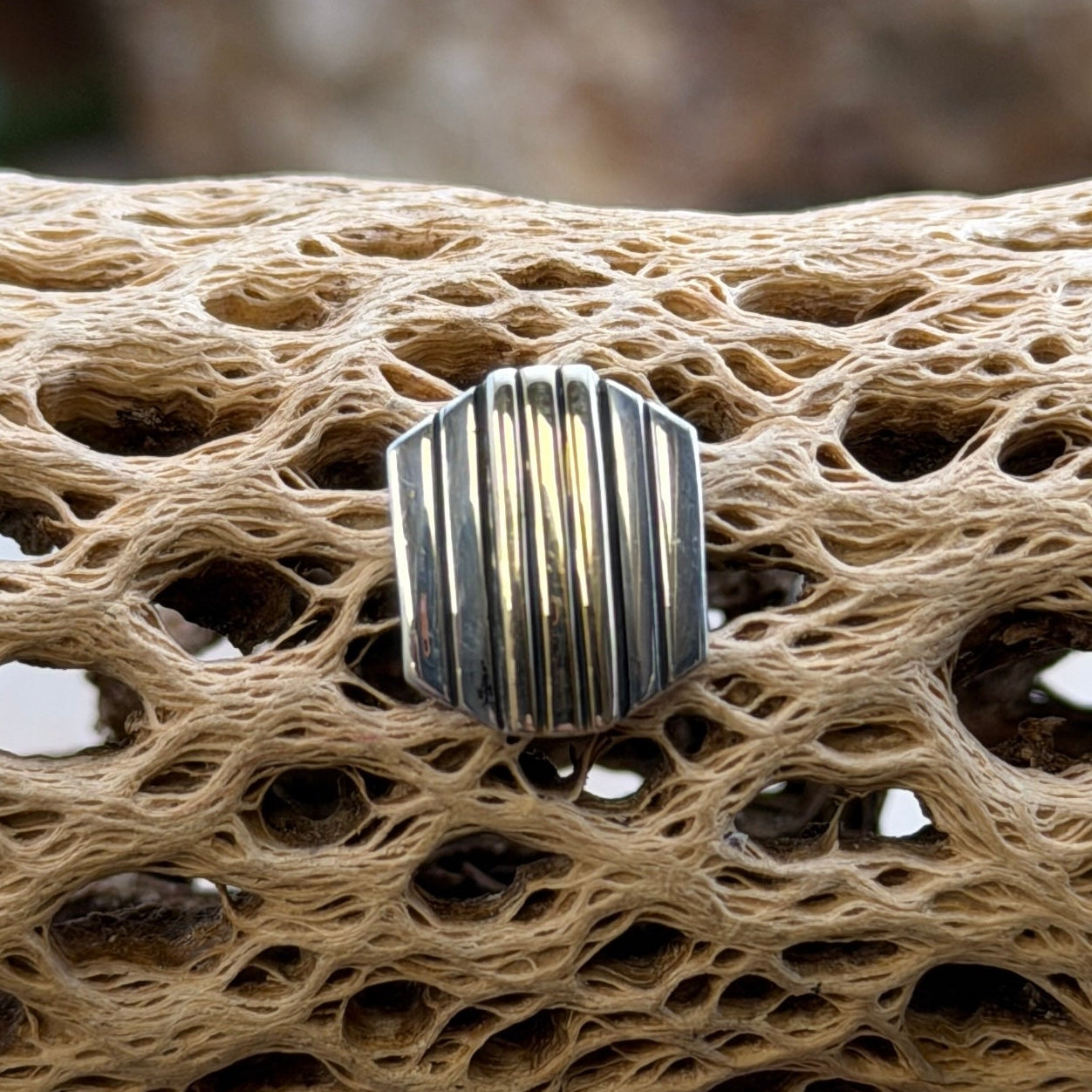 A tie tac with parallel lines of sterling silver and 14k gold on a piece of driftwood
