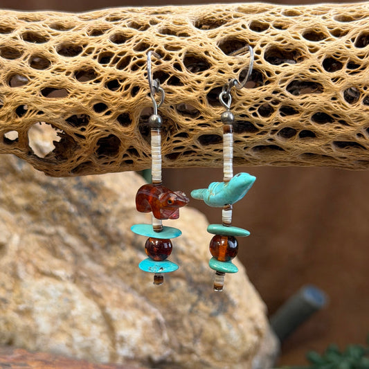 A pair of dangle earrings with cream colored heishi beads that feature two distinct animals cut from stone. on one earing a turquoise colored bird, on the other a amber colored otter. Each earring ends with a simple three item pattern of turquoise, amber, and turquoise.