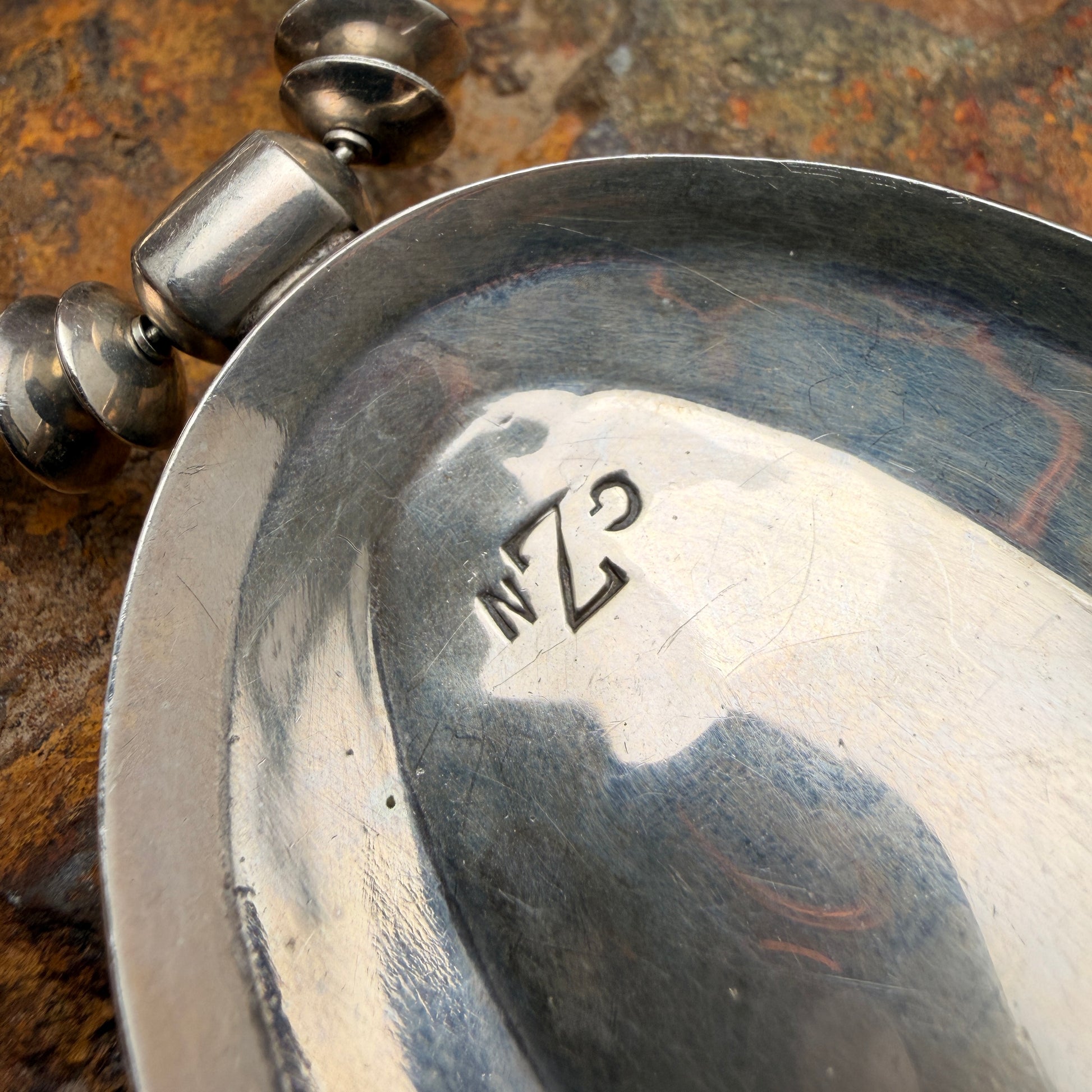 Close-up of a silver pendant with engraved initials  GZN on a textured surface