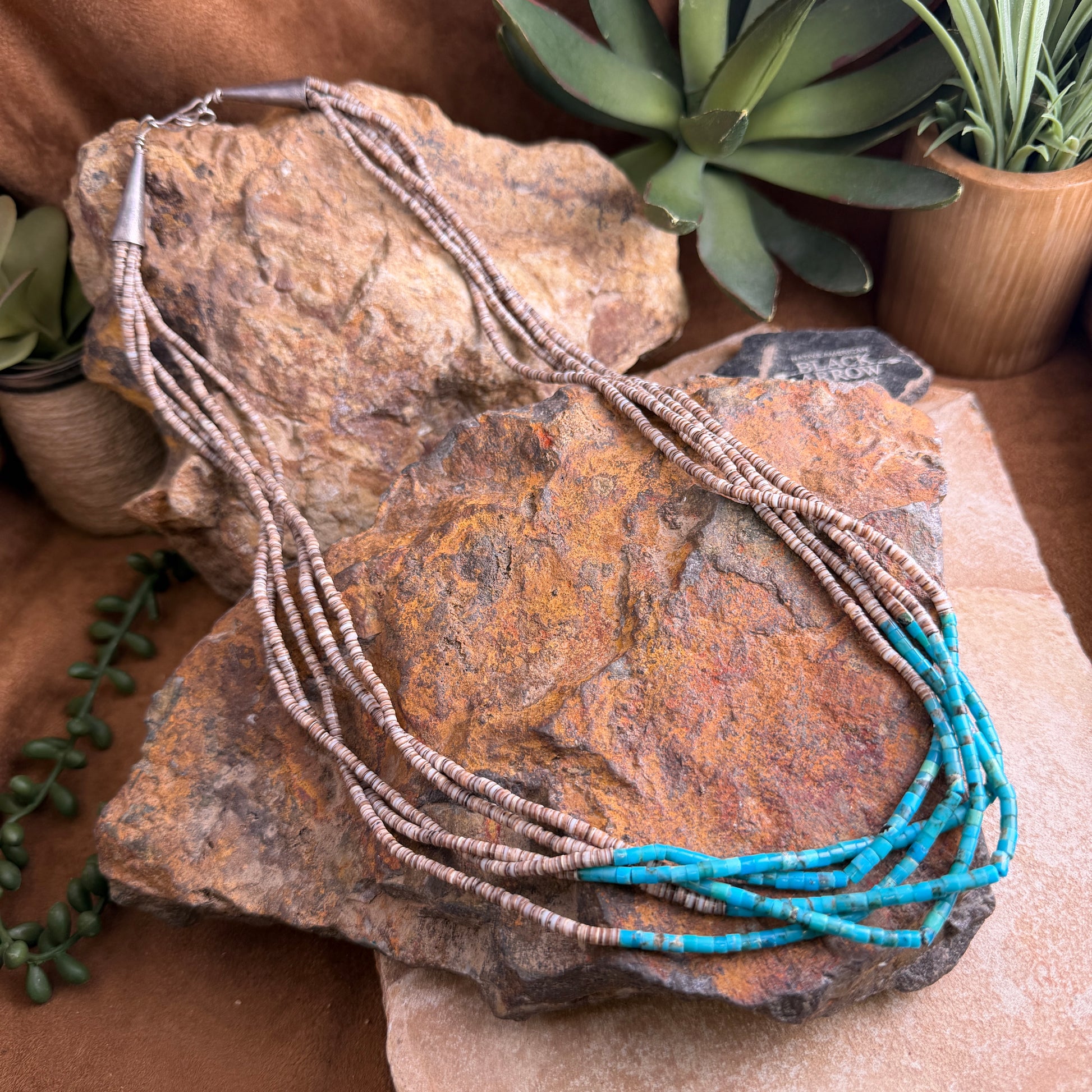 Necklace with blue and brown beads on a rock with plants in the background