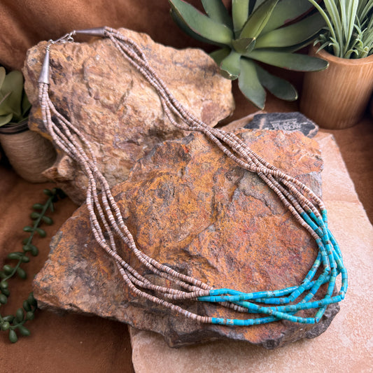 Necklace with blue and brown beads on a rock with plants in the background