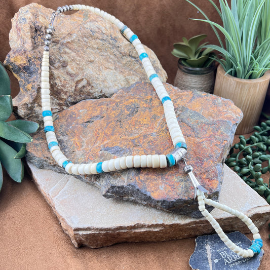 Necklace with white and blue beads on a rock with plants in the background
