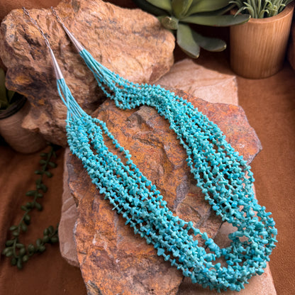 Turquoise beaded necklace on a textured stone surface with plants in the background