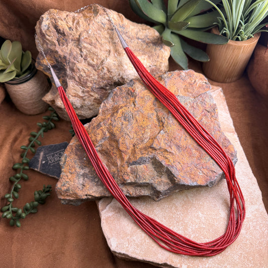 Red necklace on a stone surface with plants in the background
