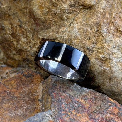 A black and silver striped band ring resting on textured orange-brown rocks.