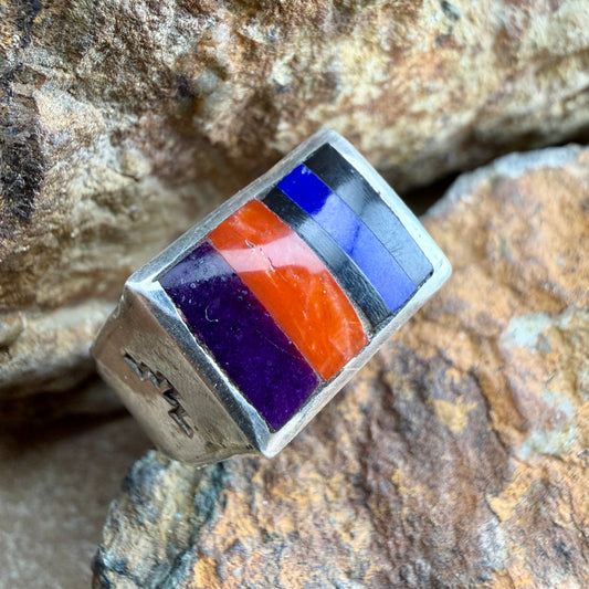 Silver ring with colorful stone inlay on a rocky surface