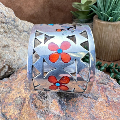 Silver cuff bracelet with red flower designs on a stone surface