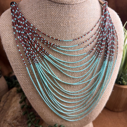 Necklace with turquoise and brown beads on a beige fabric stand.