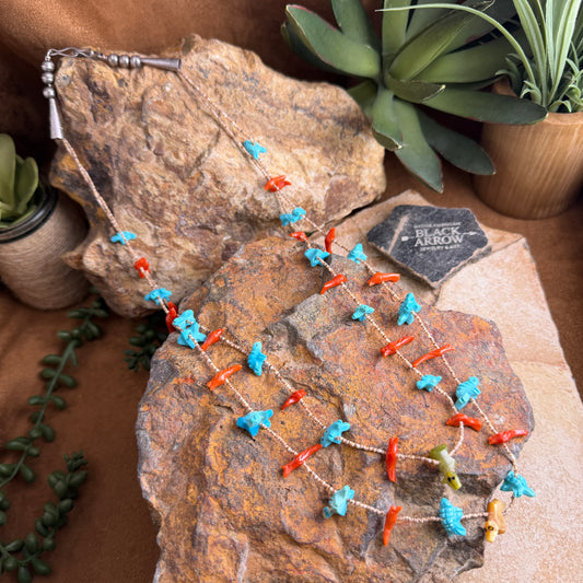 Necklace with blue and orange beads on a textured stone surface with plants in the background