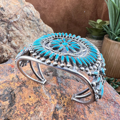 Silver and turquoise bracelet on a stone surface with a plant in the background