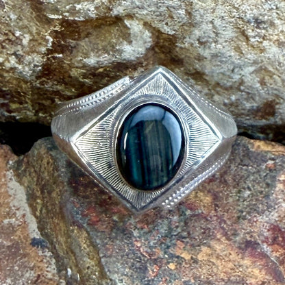 A silver-toned ring with a large oval black stone, photographed resting on textured rocks.