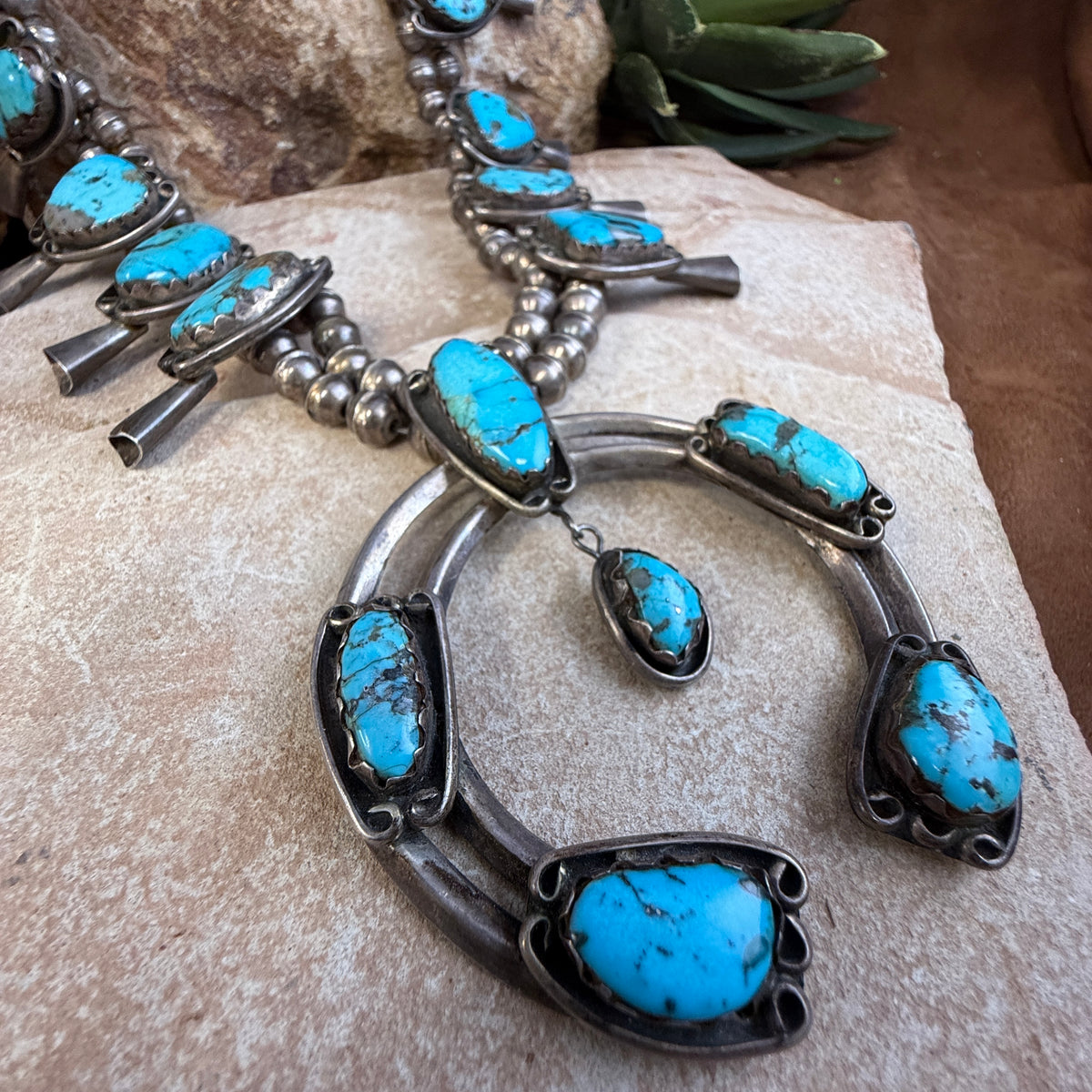 28 inch sterling silver squash blossom with blue-green turquoise and a substantial naja sitting on a rock. 