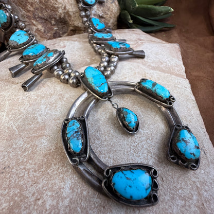 28 inch sterling silver squash blossom with blue-green turquoise and a substantial naja sitting on a rock. 