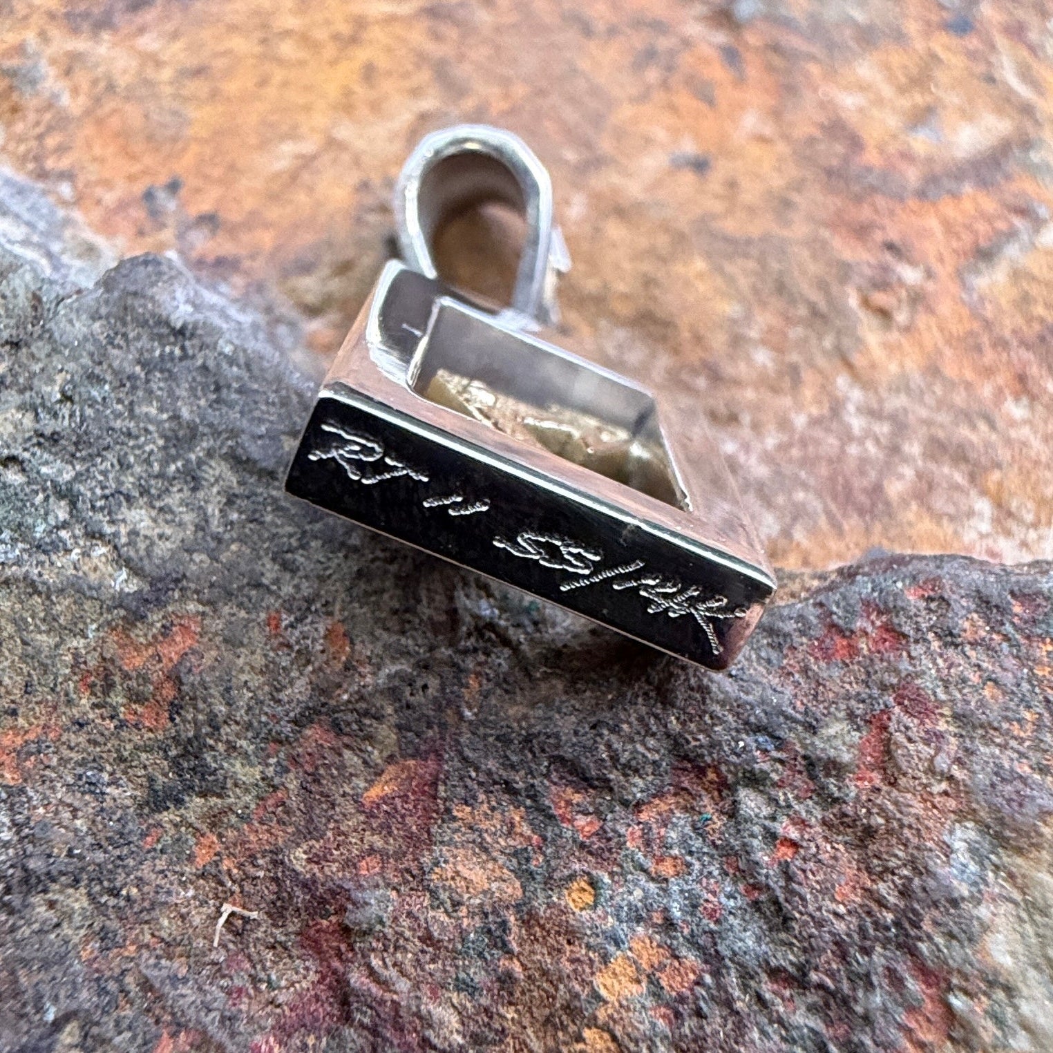 The bottom of a pendant that displays etched "RT" "ss/14k"